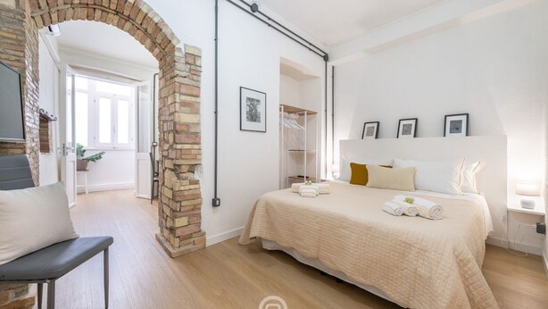 Quarto com uma cama grande, um arco de tijolos, um guarda-roupa e uma escrivaninha com abajur.