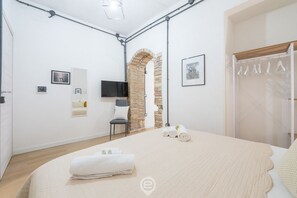 Moderni makuuhuone, jossa on suuri sänky, televisio, tuoli ja tiilestä tehty holvikaari.