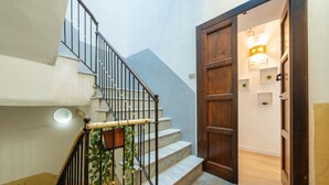 Escada com corrimão de madeira e porta que dá para um aposento com luminária e prateleiras.