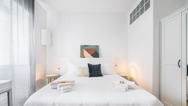 Un dormitorio ordenado con una cama grande, mesitas de noche, una obra de arte en la pared y un armario.