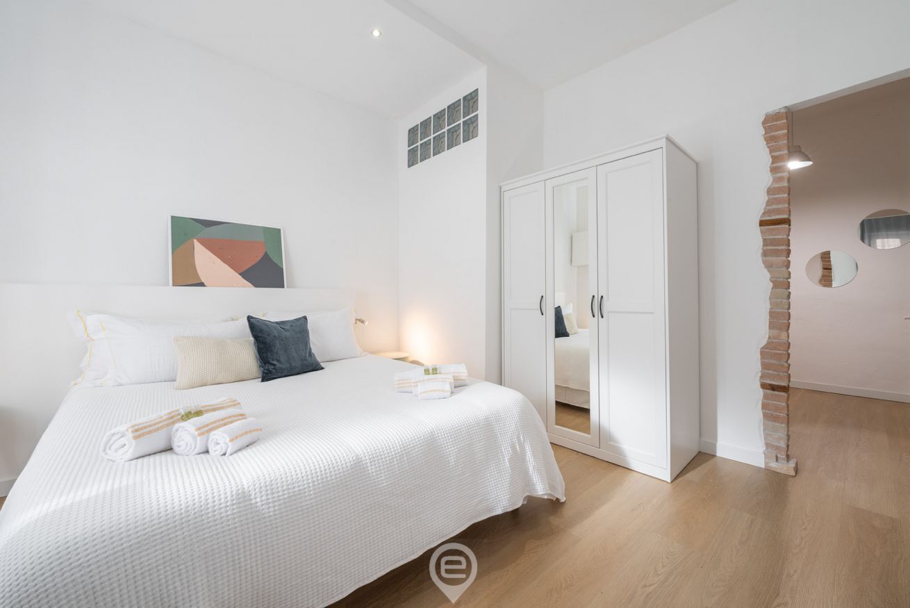 Un dormitorio moderno con una cama grande, paredes blancas y una pared de ladrillo decorativa.