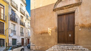Vista de una calle con un edificio que presenta una gran puerta de madera y una escalera de piedra que lleva a la entrada.