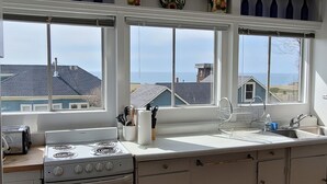 A kitchen with a stove, sink, and large windows overlooking a residential area. - Mendocino Ocean View Apartment #6 (Mendocino)