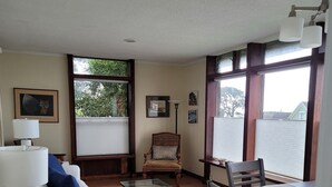 A living room with a white sofa, a glass coffee table, a dining table with chairs, and a fireplace. - Mendocino Ocean View Apartment #6 (Mendocino)