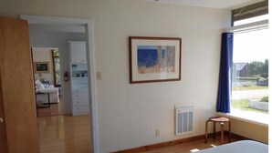 A hotel room with a bed, a small stool, a radiator, a framed picture, and a view of the outside. - Mendocino Ocean View Apartment #6 (Mendocino)