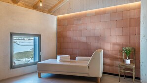 A modern room with a bed, a window, a wooden wall, and a small table with a plant. - Apartment 'Lena Dolomites Luxury Suite' with Mountain View, Private Terrace and Sauna (Villnöß)