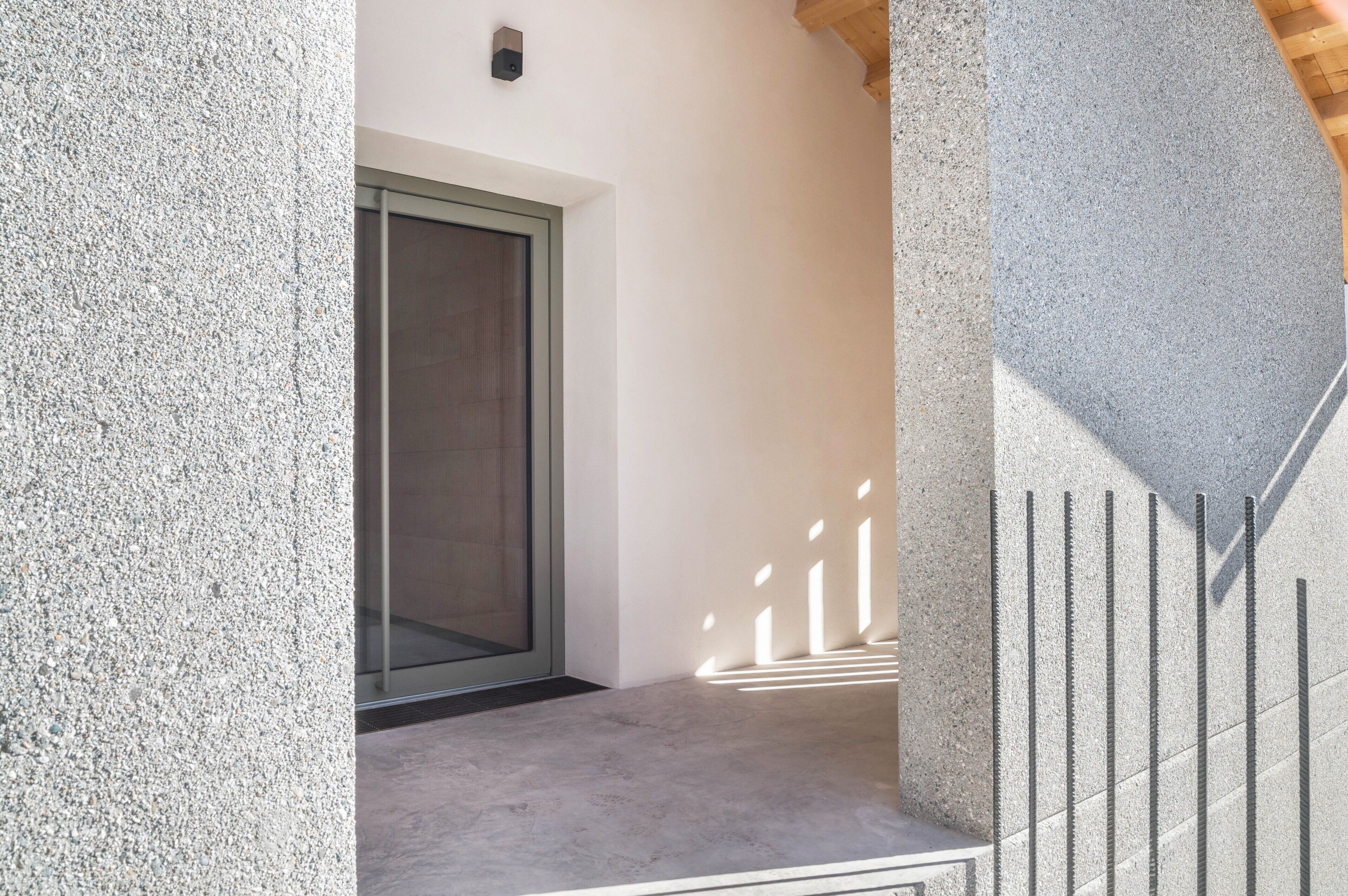 Exterior d'un edifici modern amb una paret de pedra amb textura, una porta d'estructura metàl·lica i un sòl de formigó.