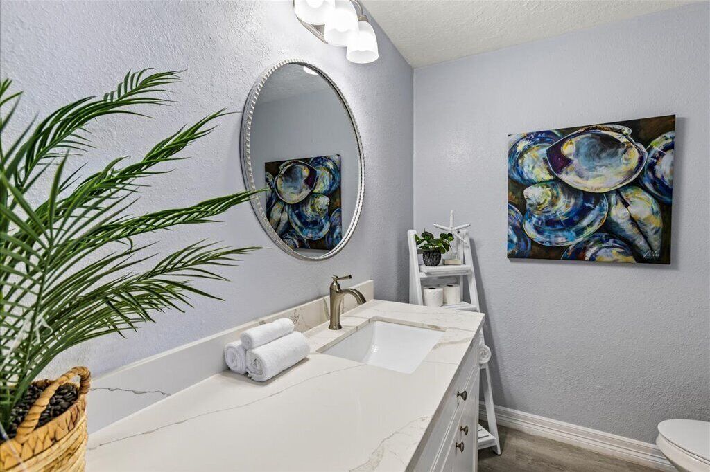 A bathroom with a white marble sink, a large mirror, and two abstract paintings on the wall.