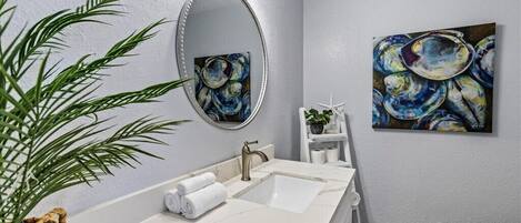 A bathroom with a white marble sink, a large mirror, and two abstract paintings on the wall.