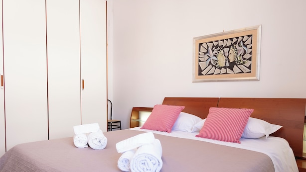 Una cama bien tendida con toallas enrolladas, un cabecero y una obra de arte enmarcada en la pared.