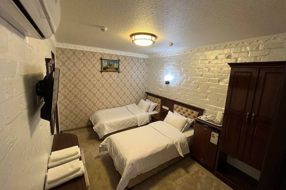 A hotel room with two beds, a wooden wardrobe, a small table, and a wall-mounted TV.
