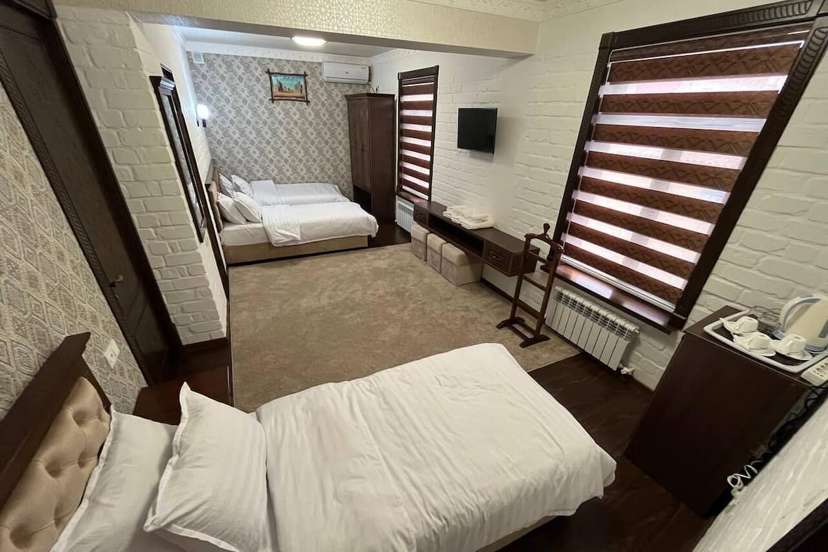 A hotel room with a bed, a desk, a chair, a radiator, and a TV mounted on the wall.