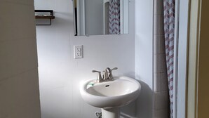 Une salle de bain avec un lavabo blanc, un miroir et un rideau de douche.