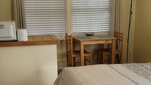 Une petite pièce agréable et chaleureuse, avec un plancher en bois, un lit recouvert d’une courtepointe à motifs, une table en bois avec des chaises, un grille-pain et une lampe.
