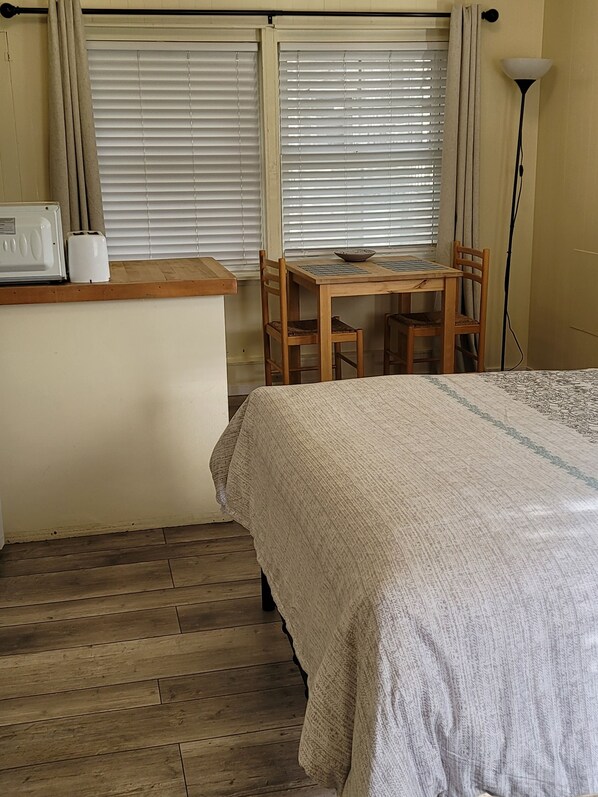 Ein kleiner, gemütlicher Raum mit Holzboden, einem Bett mit gemustertem Überwurf, einem Holztisch mit Stühlen, einem Toaster und einer Lampe.