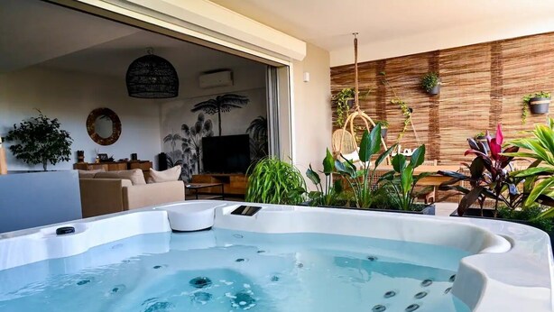 A modern outdoor hot tub area with a wooden wall and potted plants.