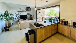A modern kitchen with a central island, wooden cabinets, and pendant lighting.