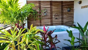 A hot tub surrounded by lush tropical plants, with a bamboo wall and a small shelf with decorative items.