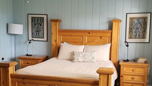 Una cama con dosel de madera con un colchón blanco y dos almohadas, flanqueada por mesitas de noche de madera con lámparas. La habitación tiene paredes de madera azul claro y suelo alfombrado.