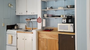 Cocina compacta con armarios blancos, encimera de madera, estufa y microondas.