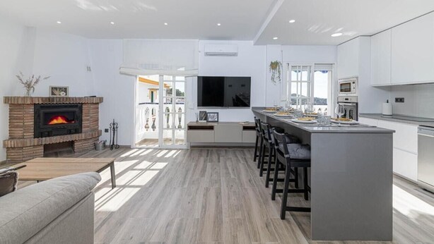 Una cocina moderna con una isla central, una chimenea empotrada y un televisor grande.