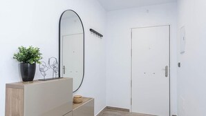 Un pasillo con piso de madera, una puerta blanca, un espejo, una planta en maceta y un armario.