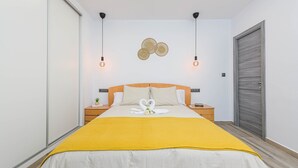 Un dormitorio ordenado con cama, mesitas de noche, una lámpara de pared y una puerta.