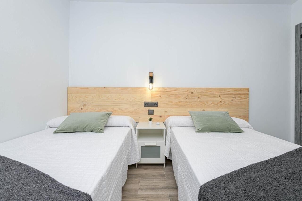 A double room with two beds, a wooden headboard, a bedside table with a lamp, and a small plant.