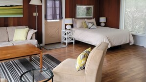 A modern bedroom with a wooden floor, a bed, a sofa, a coffee table, and a painting on the wall. - Mendocino 2nd Floor Studio #7 in the Village, full kitchen (Mendocino)