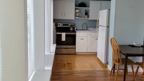 A compact kitchen with white cabinets, a stove, a sink, and a refrigerator. There is a wooden dining table with two chairs. - Mendocino 2nd Floor Studio #7 in the Village, full kitchen (Mendocino)