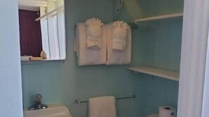 A small, compact bathroom with a sink, toilet, and a mirror. There are two towels hanging on the wall and a shelf above the toilet. - Mendocino 2nd Floor Studio #7 in the Village, full kitchen (Mendocino)