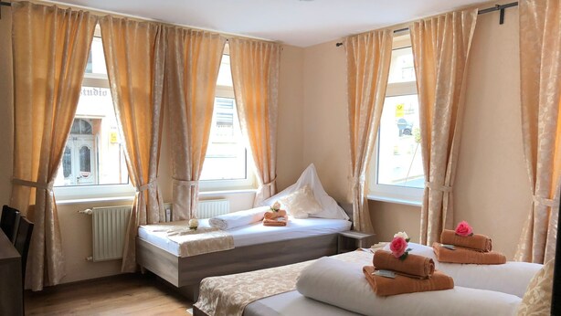 A hotel room with two beds, a window with curtains, a radiator, and a small table. - Pension Goldenes Vogtland (Adorf)