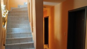 Una escalera que lleva a una puerta oscura, con suelo de baldosas y un pequeño tapete al final.