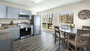 A modern kitchen with grey cabinets, stainless steel appliances, and a dining area with wooden chairs and a table. - White Oak Landing Spacious 6 BDR w/ Boat Slip! (Sunrise Beach)