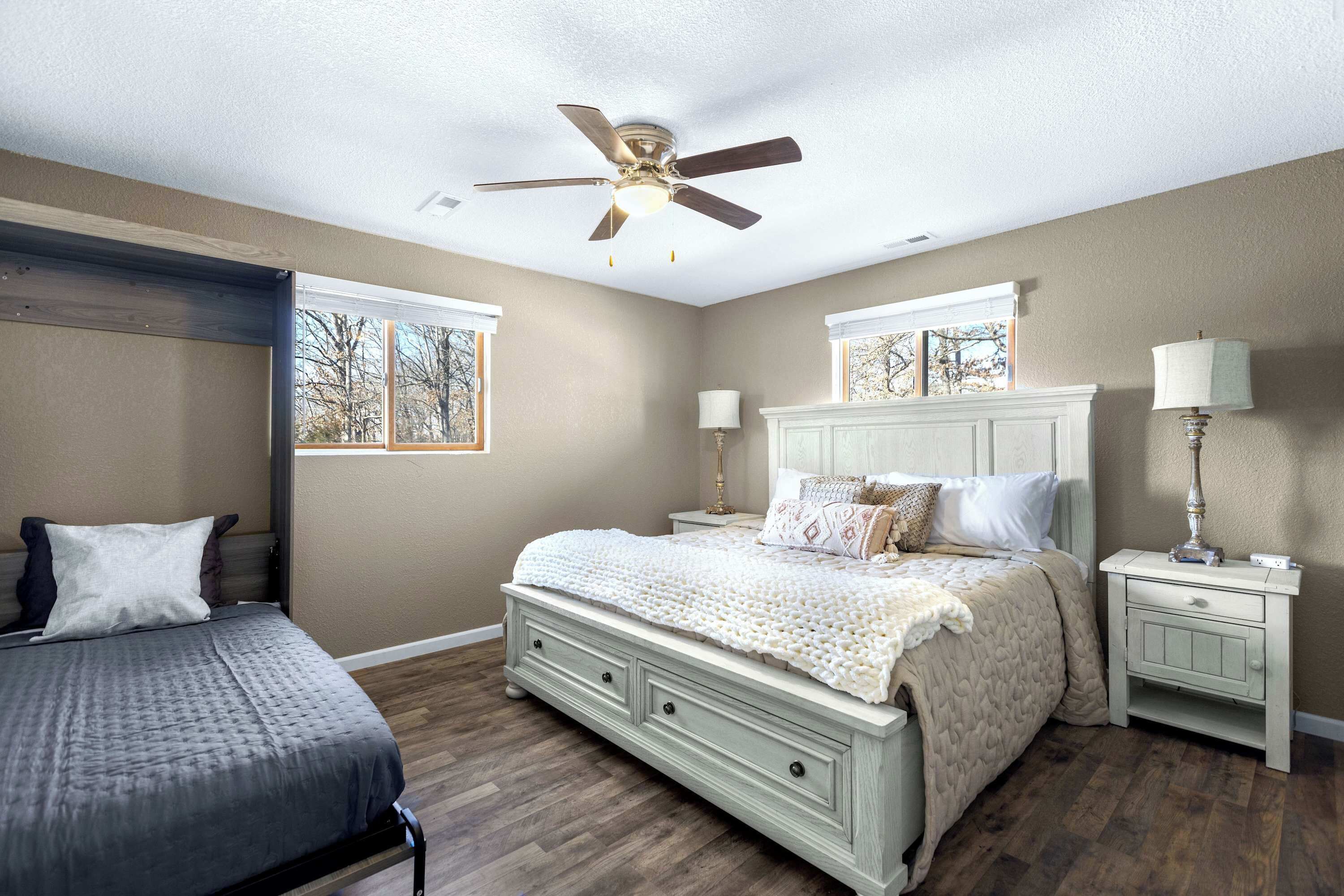 A bedroom with a bed, a nightstand, a ceiling fan, and a window with a view of trees.