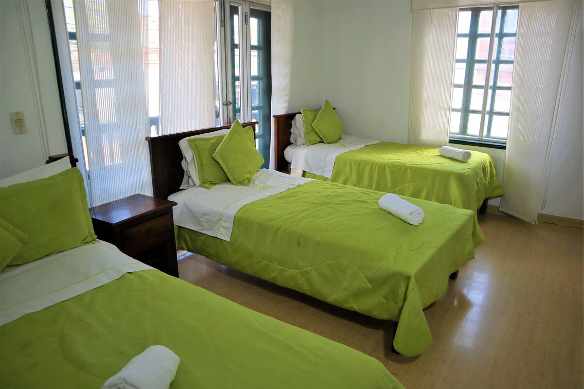 Een hotelkamer met drie enkele bedden, elk met groen beddengoed en witte kussens, en een houten hoofdbord.