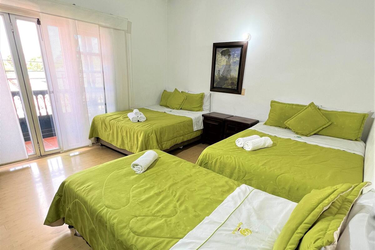 Hotelkamer met twee bedden, elk voorzien van groen beddengoed en witte kussens, een schilderij aan de muur en een schuifdeur naar een buitenruimte.