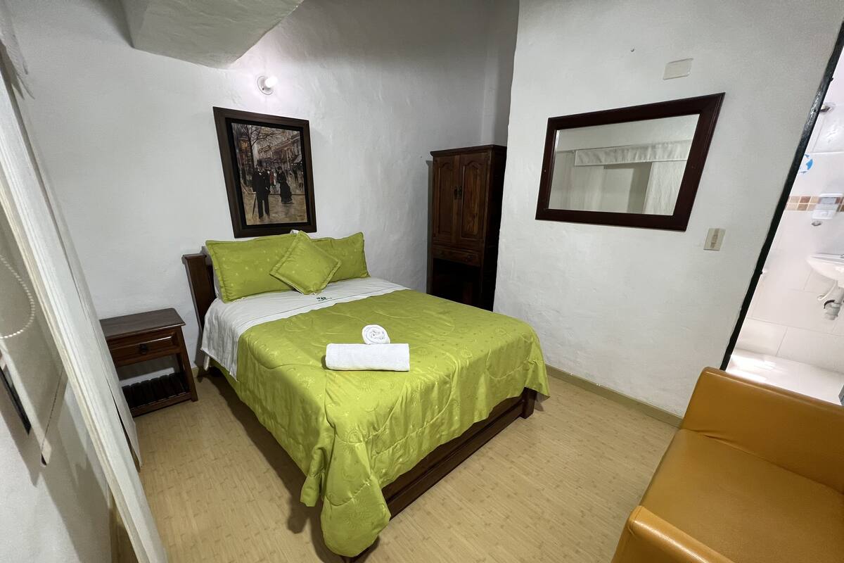 Een slaapkamer met een bed, nachtkastje, houten kledingkast, spiegel en een badkamer die door een open deur zichtbaar is.