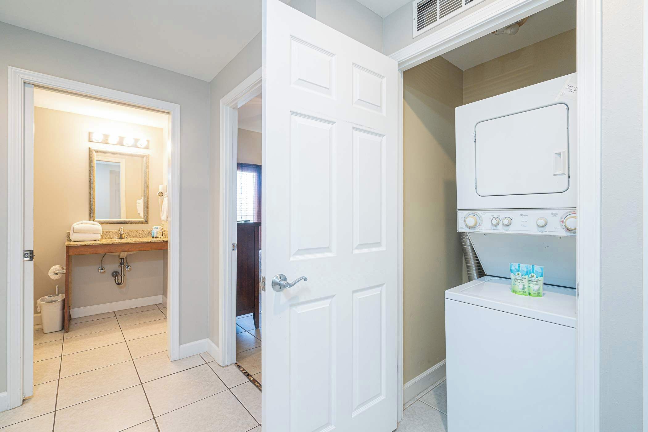 A bathroom with a vanity, a mirror with lights, a door, and a washing machine.
