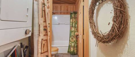 Een wasruimte met een wasmachine, een houten deur naar een badkamer met toilet en douche, en een krans aan de muur.