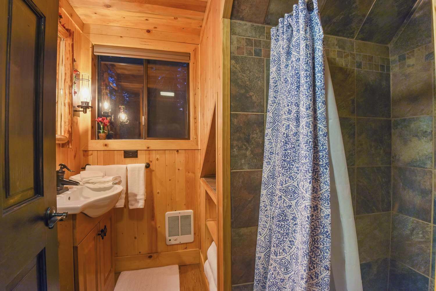 A wooden bathroom with a sink, mirror, and window.