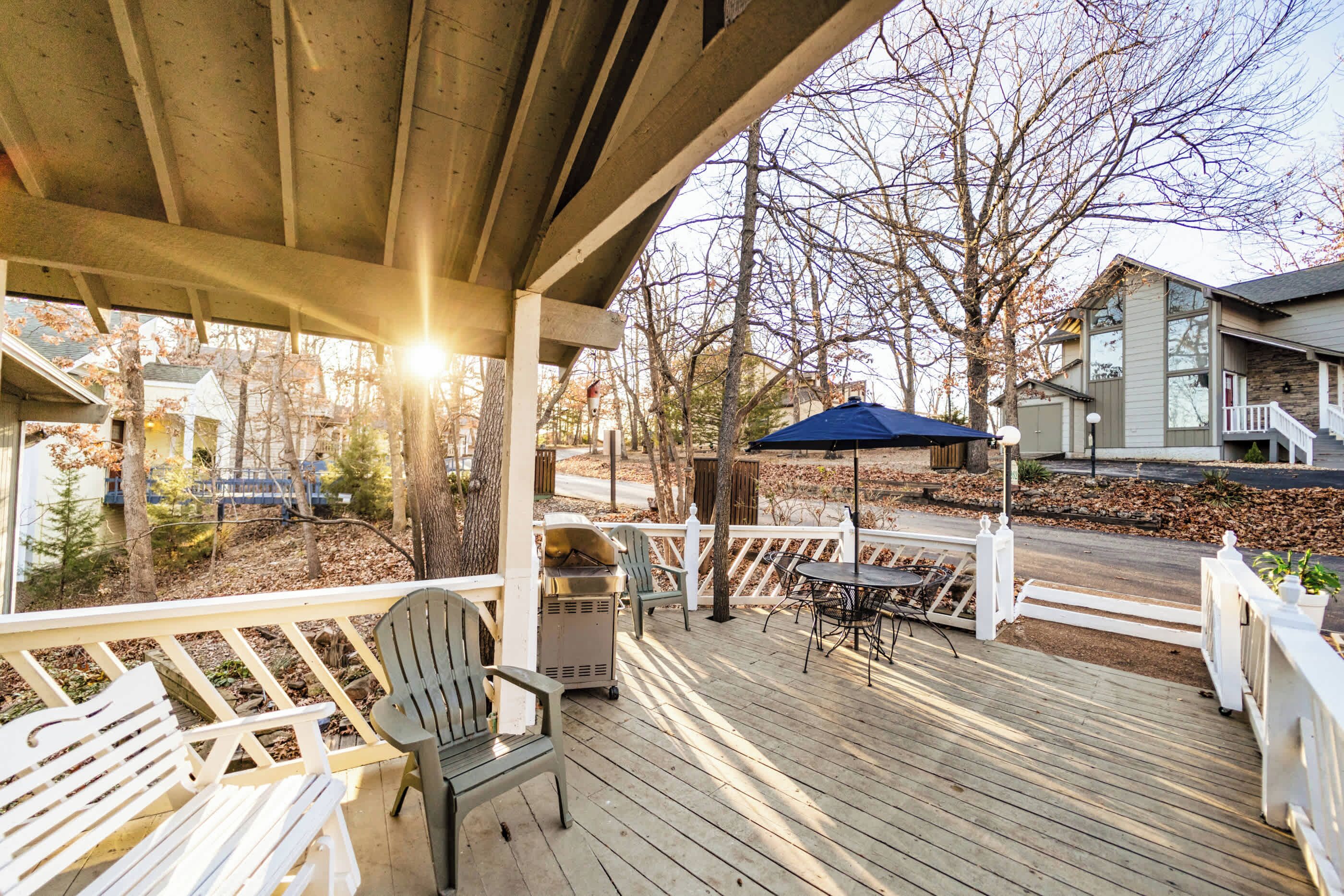 Eine Holzterrasse mit Gartenmöbeln, einem Grill und einem blauen Sonnenschirm.