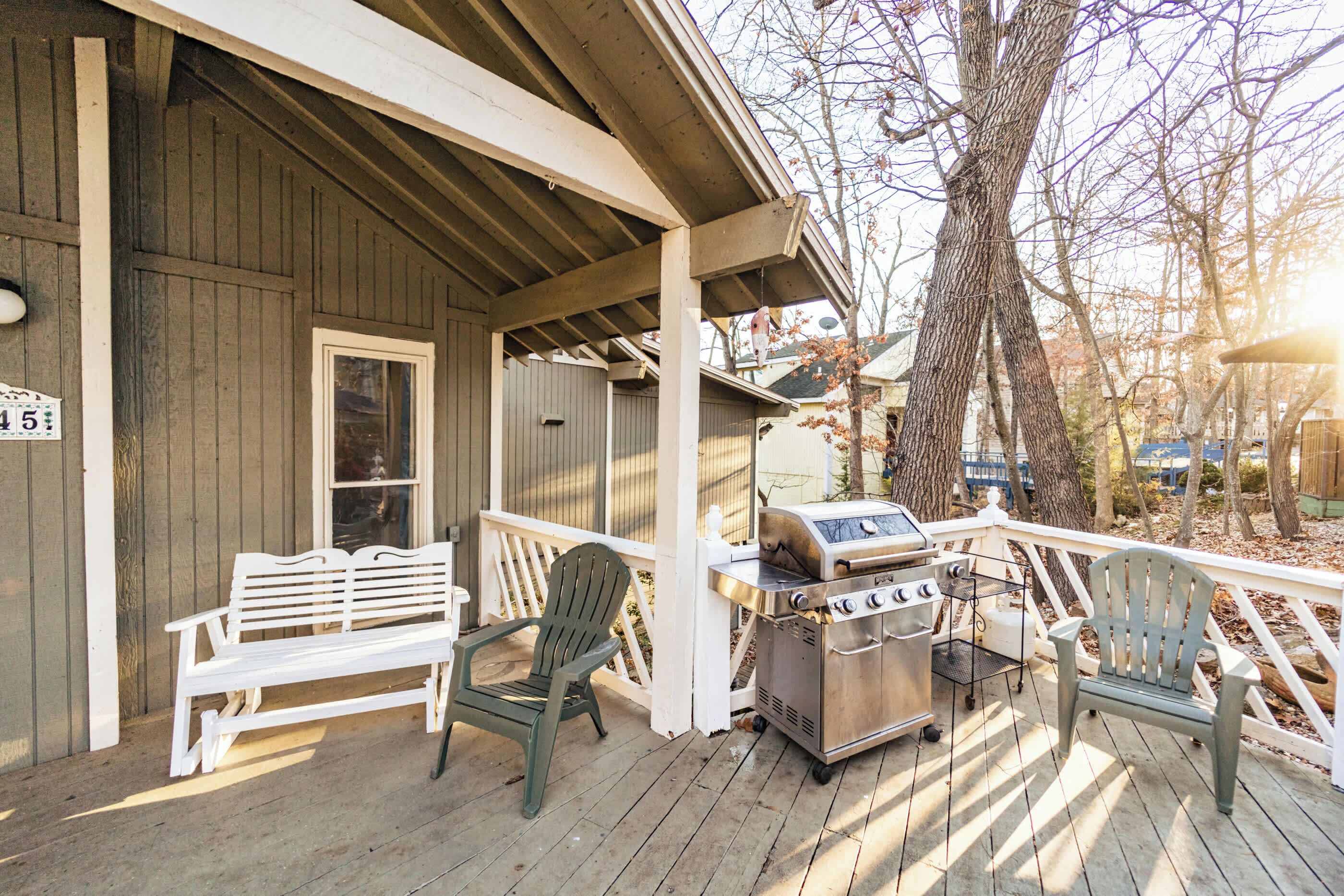 A wooden deck with a grill, two white benches, and a chair.