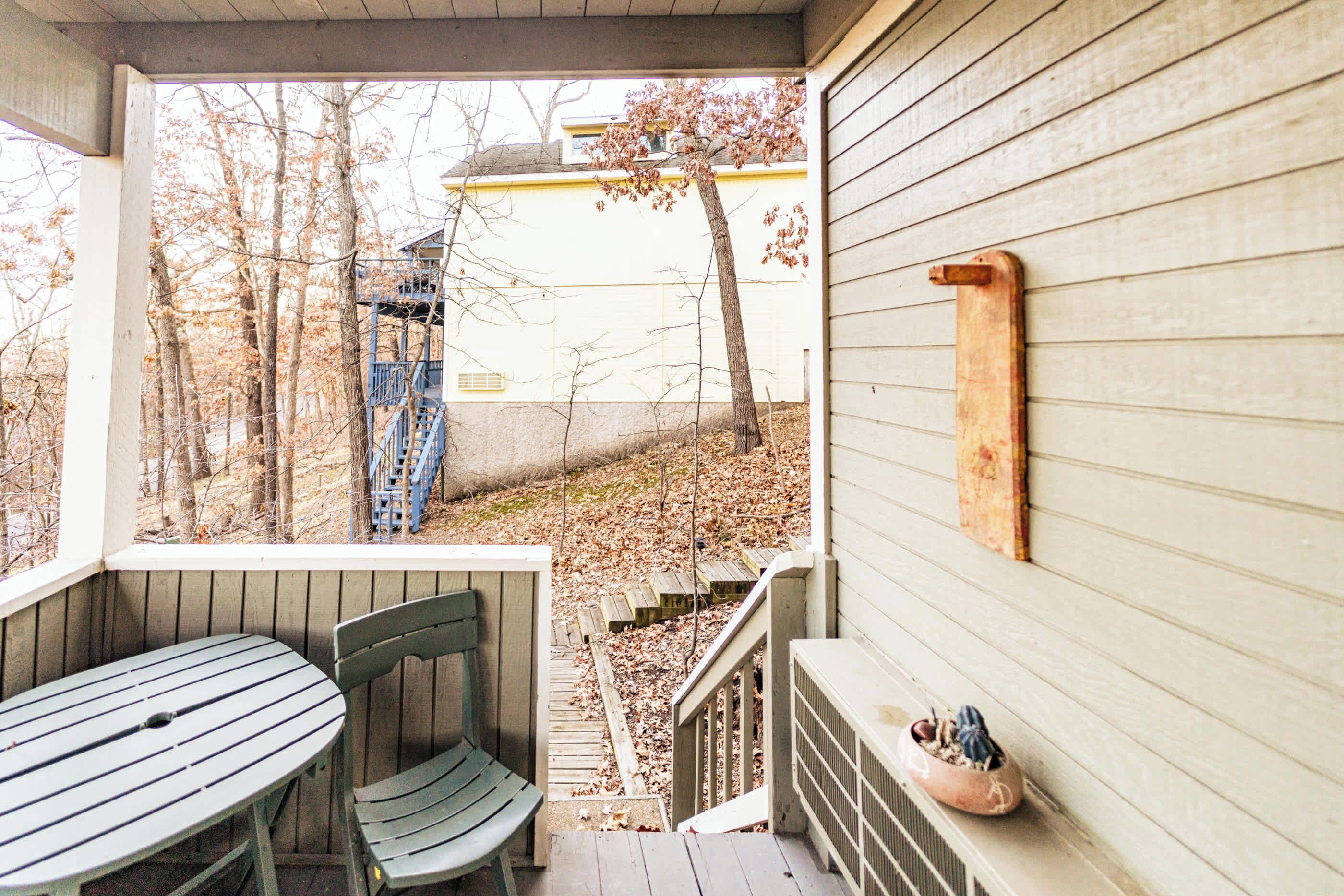 A wooden deck with a table and chairs, a small staircase, and a view of a building and trees.
