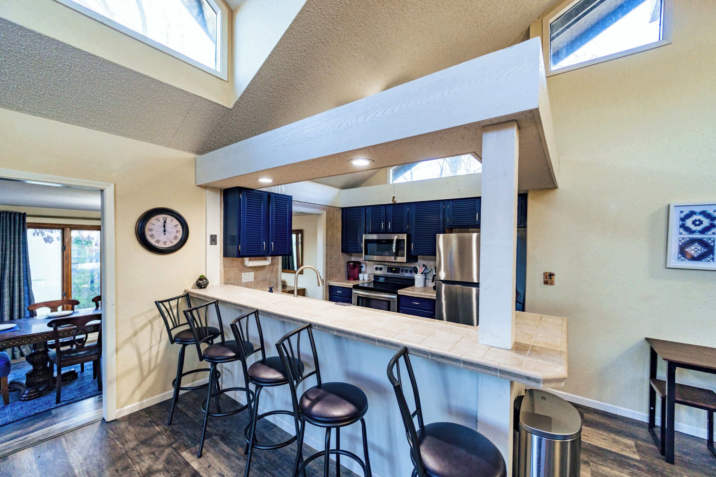 A modern kitchen with a bar area, dark blue cabinets, stainless steel appliances, and a clock on the wall.