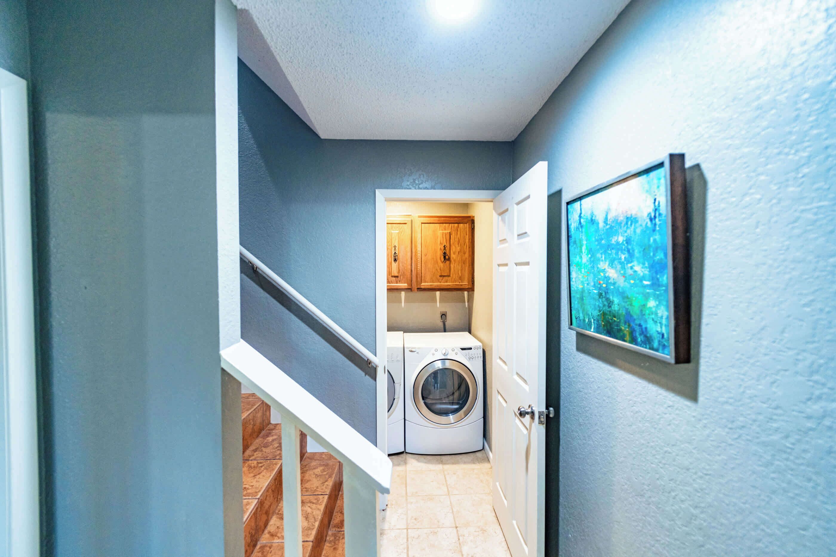 A laundry room with a washing machine and dryer, wooden cabinets, and a framed picture on the wall.