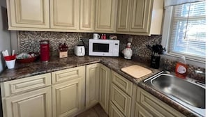 Una cocina con gabinetes color crema, microondas, tostadora y pileta.
