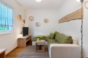 A modern living room with a flat-screen TV, a green sofa, a white armchair, and a small table with books.