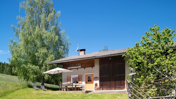 A rustic building with a sign reading 'Ödenhof,' a covered outdoor seating area, and a large tree in the background.