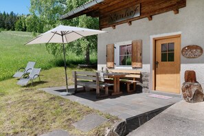 Un bâtiment en bois avec un banc et une table à l’extérieur, une porte et une enseigne.